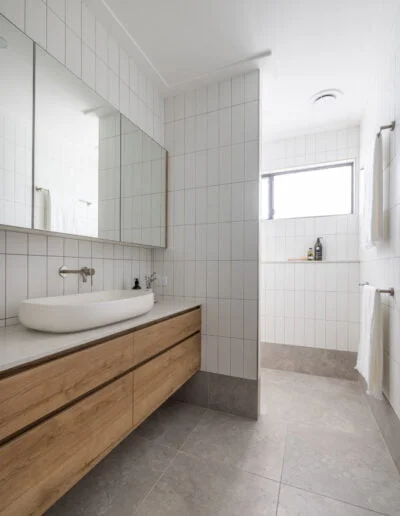 Contemporary bathroom with grey marbled floors, white subway walls, timber vanity and mirror cabinet.