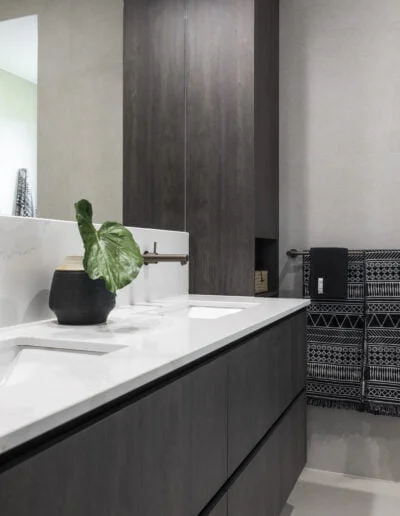 Modern luxurious bathroom with dark timber vanity, bronze taps and warm grey floor tiles.