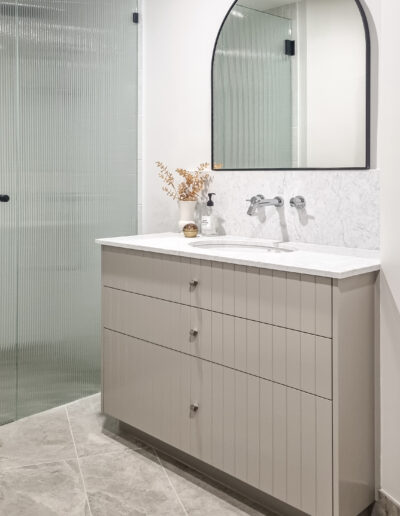 Modern vintage bathroom in warm greys with VJ vanity, arched mirror and fluted glass shower screen.